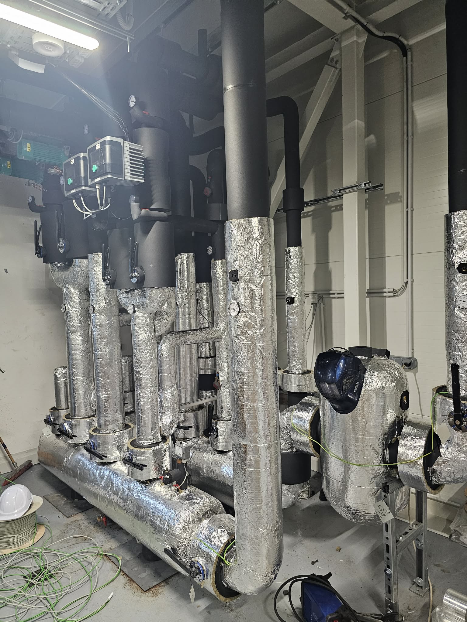 Hospital corridor ceiling with exposed insulated HVAC ducts and pipes showing professional medical facility grade insulation installation