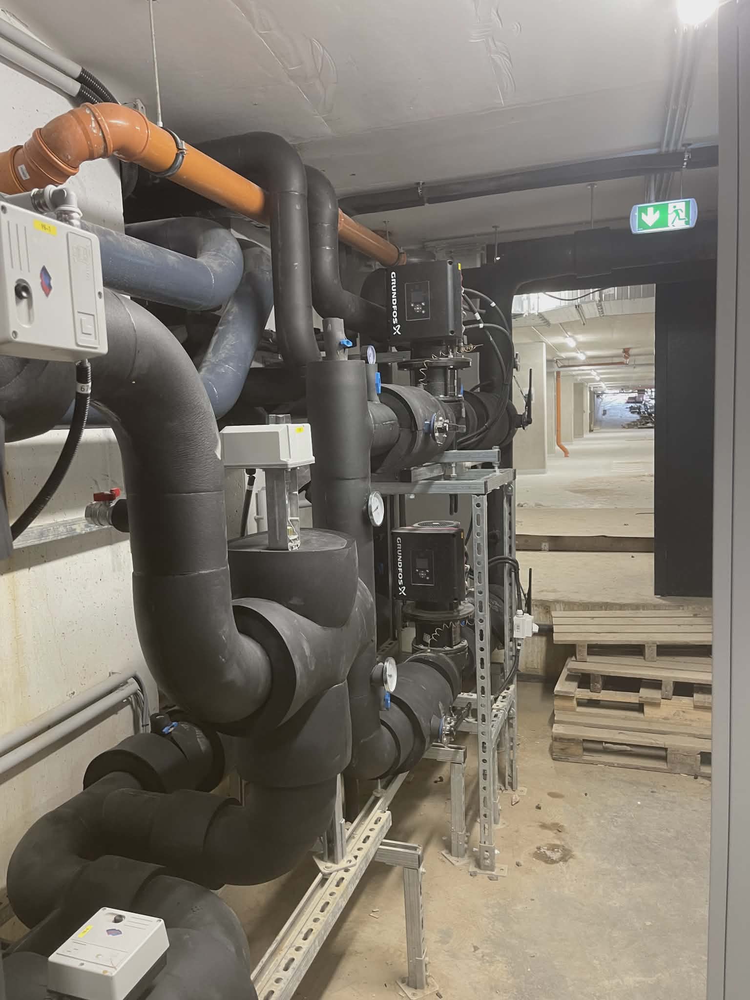 Modern residential building basement showing insulated heating pipes and distribution manifolds with professional orange and white insulation wrapping